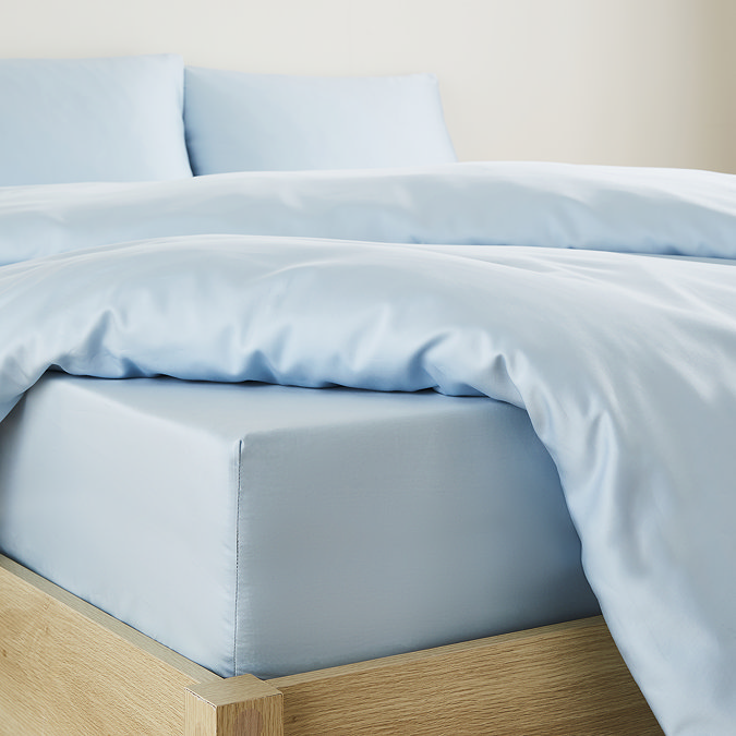 close-up on corner of bed with light blue fitted sheet over the mattress, matching duvet set pulled back to reveal fit, and matching pillowcases