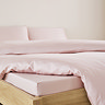close-up on corner of bed with pale pink fitted sheet over the mattress, matching duvet set pulled back to reveal fit, and matching pillowcases