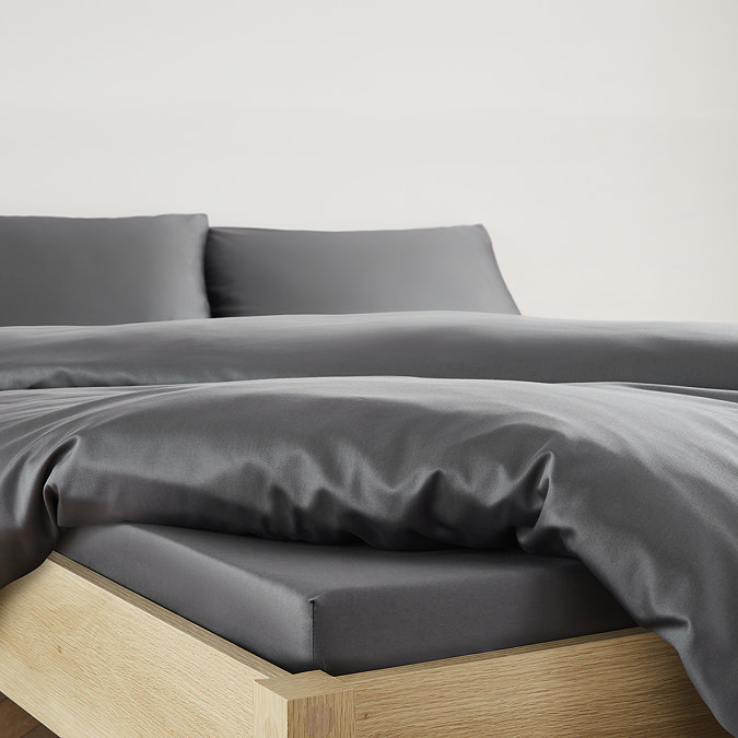 close-up on corner of bed with charcoal grey fitted sheet over the mattress, matching duvet set pulled back to reveal fit