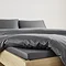 close-up on corner of bed with charcoal grey fitted sheet over the mattress, matching duvet set pulled back to reveal fit