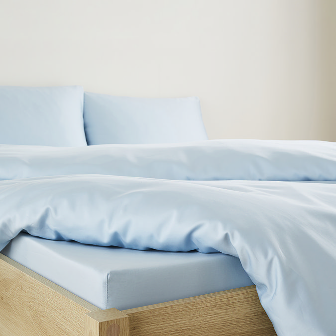 close up on corner of bed with mattress covered in light blue fitted sheet, standard size, matching coloured duvet pulled back at the end to reveal the sheet fit