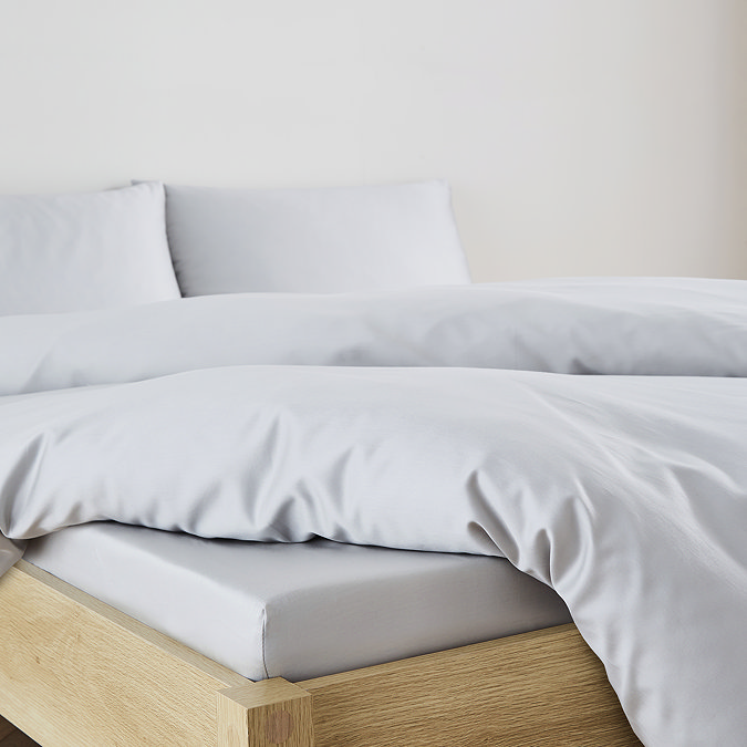 close-up on corner of bed with silver fitted sheet over the mattress, matching duvet set pulled back to reveal fit, and matching pillowcases