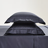 two pillows in dark blue pillowcases stacked one on top of the other on matching flat sheet