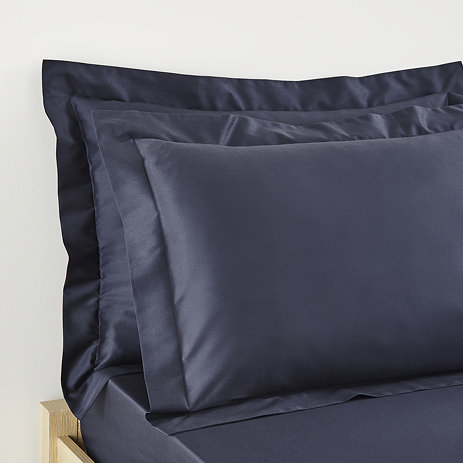 close up on pillows in dark blue oxford border pillowcases at head of bed