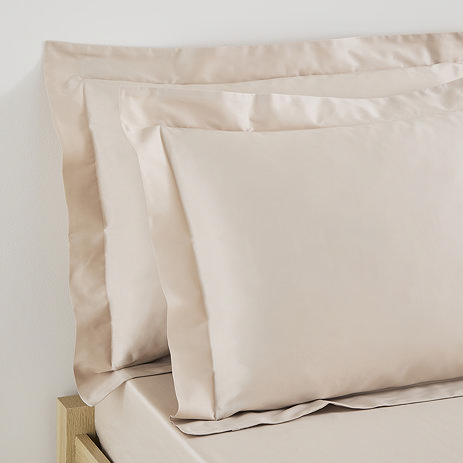 close up on two pillows in natural coloured oxford pillowcases propped up at the head of a bed