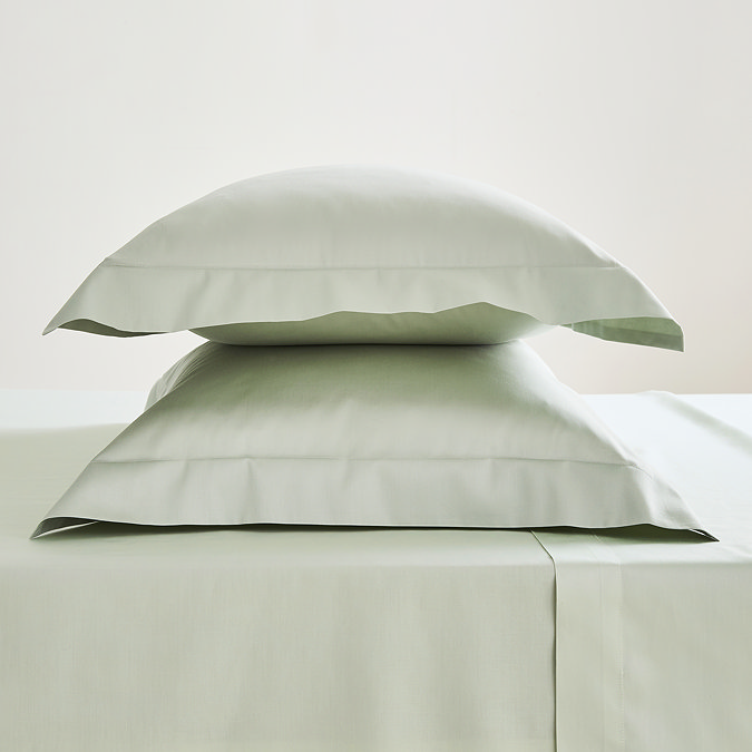 two sage green oxford pillowcases filled and stacked one on top of the other on matching fitted sheet