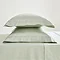 two sage green oxford pillowcases filled and stacked one on top of the other on matching fitted sheet