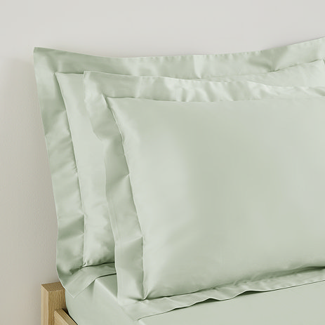 close up on two pillows in sage green oxford border pillowcases propped up at head of bed