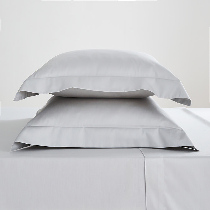 pair of pillows in silver pillowcases stacked one on top of the other on matching flat sheet