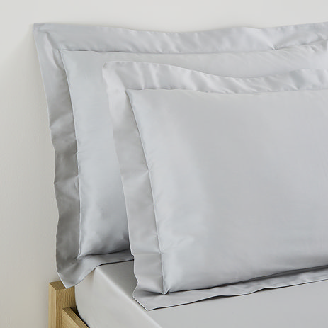 close up on pair of pillows in silver grey pillowcases propped up at the head of a bed
