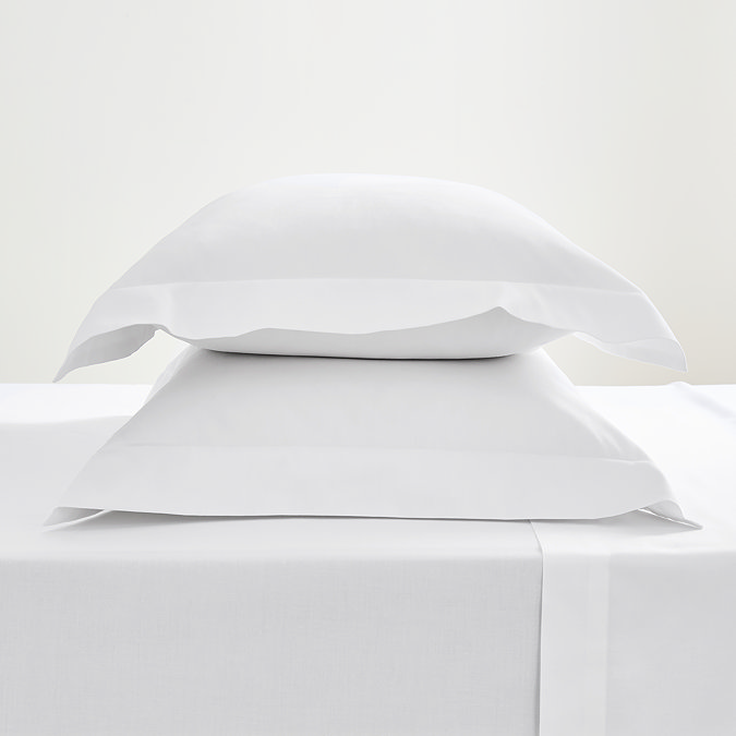 pair of pillows in white oxford pillowcases stacked one on top of the other non top of a flat white sheet