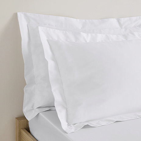 close up on pair of pillows in white oxford pillowcases propped up at head of bed