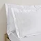 close up on pair of pillows in white oxford pillowcases propped up at head of bed