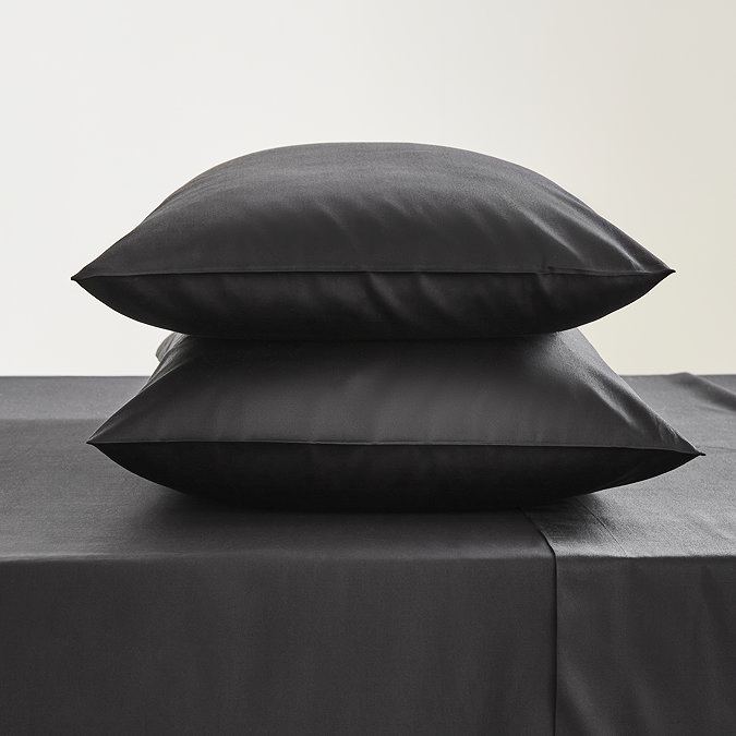 two pillows in black pillowcases stacked one on top of the other, on a matching black fitted sheet