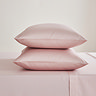 two pillows in blush pink pillowcases stacked one on top of the other, on a flat sheet