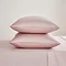 two pillows in blush pink pillowcases stacked one on top of the other, on a flat sheet