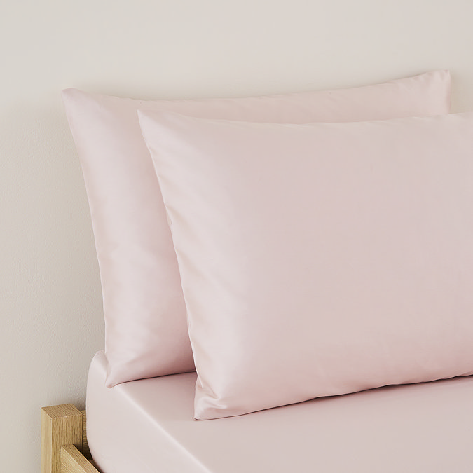 close up on pair of pillows in blush pink pillowcases, at top of bed with matching pink fitted sheet