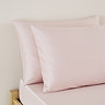 close up on pair of pillows in blush pink pillowcases, at top of bed with matching pink fitted sheet