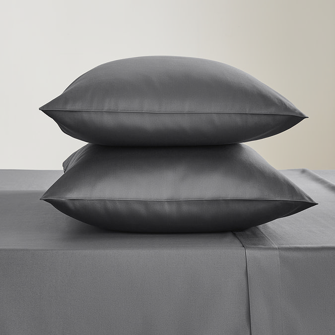 two pillows in charcoal grey pillowcases stacked one on top of the other on a matching grey flat sheet