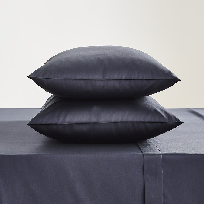 pair of pillows in dark blue pillowcases stacked one on top of the other on matching flat sheet