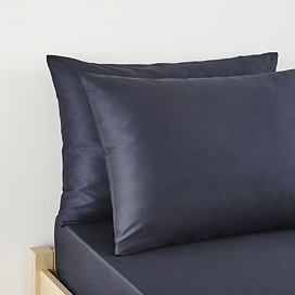 close up on pair of pillows in dark blue pillowcases at head of bed
