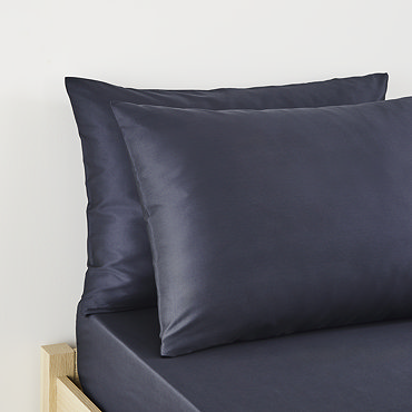 pair of pillows in dark blue pillowcases stacked one on top of the other on matching flat sheet