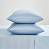 two pillows in light blue pillowcases stacked one on top of the other on top of matching blue flat sheet