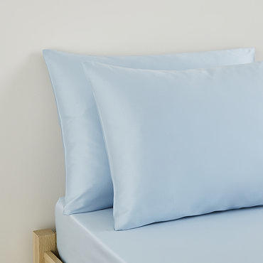 two pillows in light blue pillowcases stacked one on top of the other on top of matching blue flat sheet