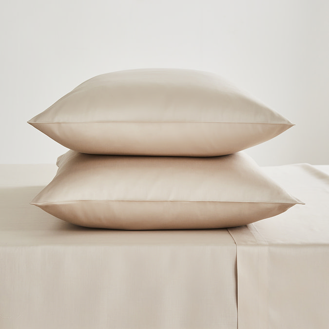 two pillows in natural coloured pillowcases stacked one on top of the other on a matching flat sheet