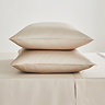 two pillows in natural coloured pillowcases stacked one on top of the other on a matching flat sheet