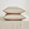 two pillows in natural coloured pillowcases stacked one on top of the other on a matching flat sheet