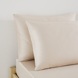 close up on pillows in natural coloured pillowcases at top of bed