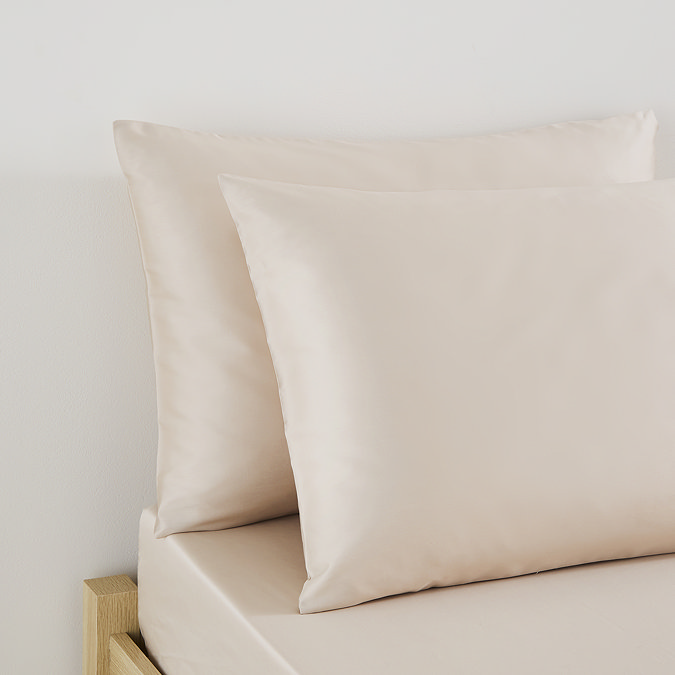 close up on pillows in natural coloured pillowcases at top of bed
