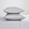 two pillows in silver pillowcases stacked one on top of the other on matching silver flat sheet