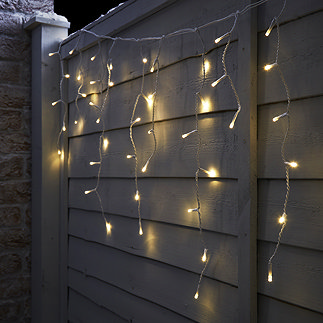 warm white hanging icicle lights on a fence, lit up at night