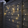 warm white hanging icicle lights on a fence, lit up at night