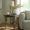 image of square rustic side table with carved legs, topped with matching lamp, next to grey upholstered sofa