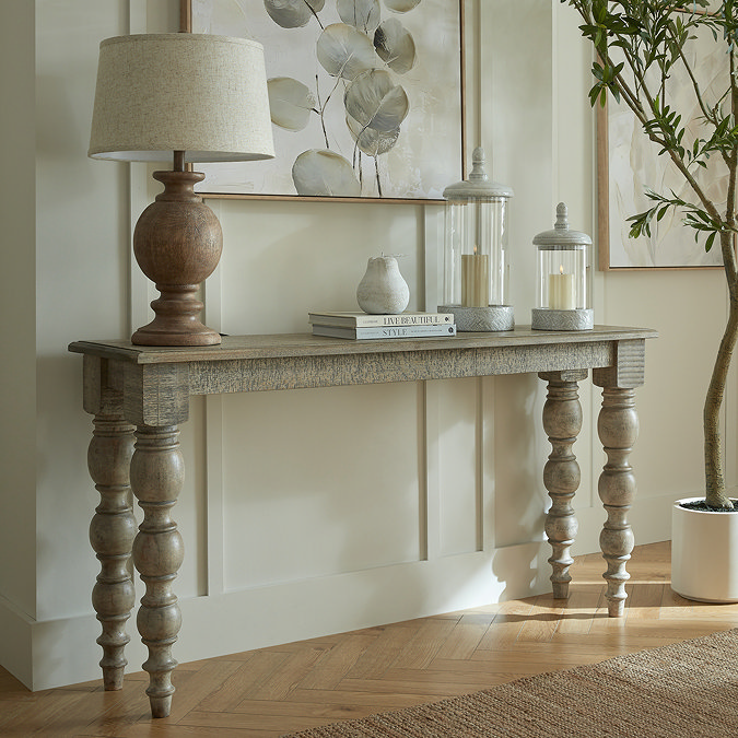 image of rustic console table with carved legs against a cream panelled wall, topped with brown lamp