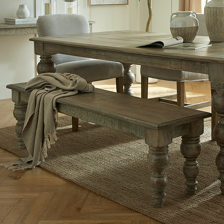 image of rustic brown dining bench with carved legs, tucked on one side of matching dining table, with brown throw draped over one end