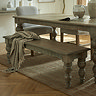 image of rustic brown dining bench with carved legs, tucked on one side of matching dining table, with brown throw draped over one end