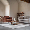 wide shot of round acacia wood coffee table in middle of living room surrounded by sofa and armchair