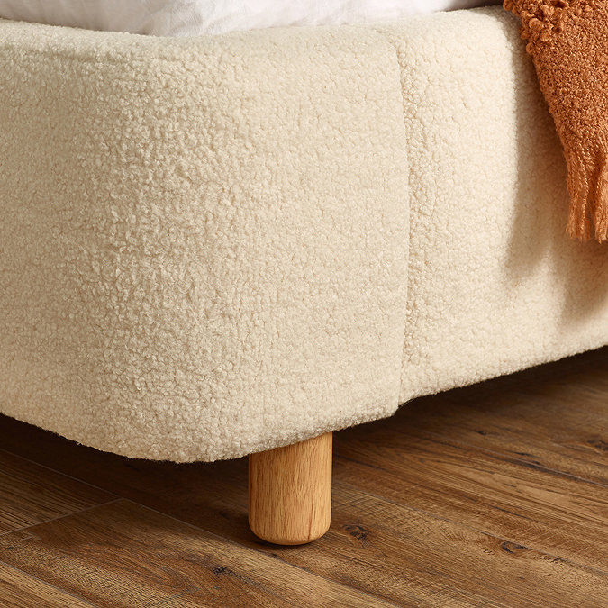 close up image on beige boucle bottom half of bed with small light wood feet