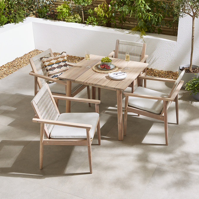image taken from slightly above of square acacia wood outdoor dining table with matching chairs and cream cushions