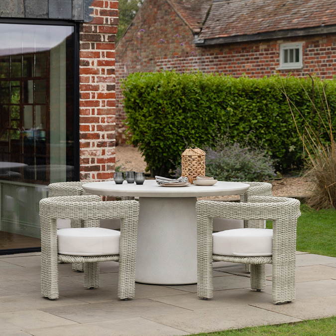 image of round cream concrete outdoor dining table with two rattan garden chairs with matching cream cushions
