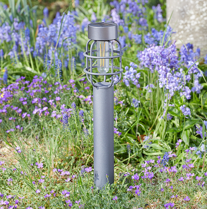image of grey lantern-style stake light in flower bed of garden during the day