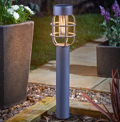 image of grey lantern-style tall stake light in garden flower bed emitting warm white light