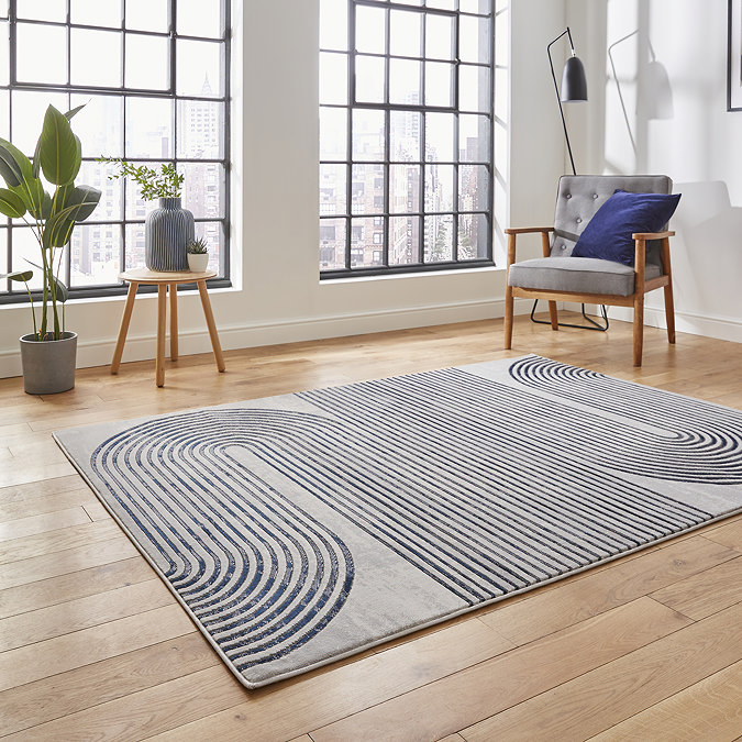 angled image of large grey rug with wavy swirl pattern in navy blue in front of modern loft window