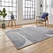angled image of large grey rug with wavy swirl pattern in navy blue in front of modern loft window