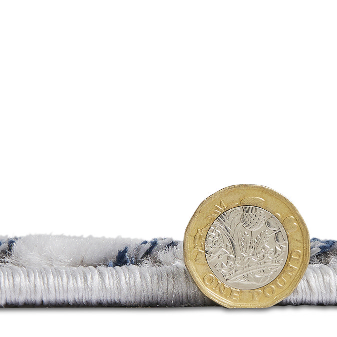 image cut out on white background of grey-blue rug next to a pound coin stood up to show rug as half the height of the coin