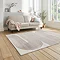 angled image of grey rectangular rug with rose coloured geometric weave, in front of cream coloured sofa with rose coloured throw